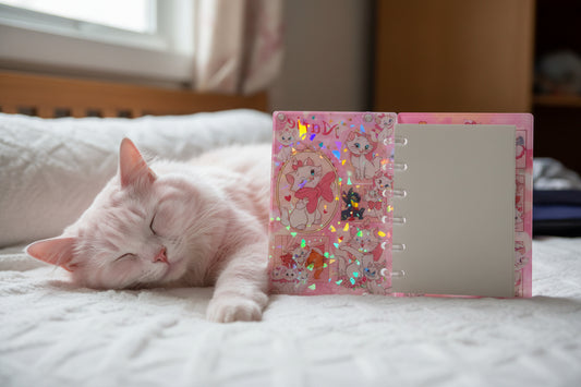 FLUFFY WHITE CAT BED WITH PINK CAT COLOR WITH NOTEBOOK STANDING UP ON BED